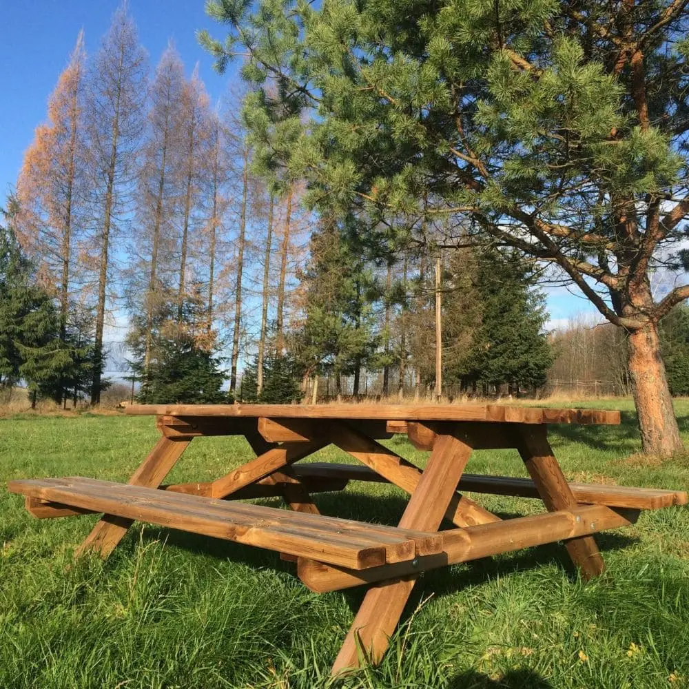 Table de pique-nique en bois massif traité autoclave pour l'extérieur, installée dans une prairie herbeuse.